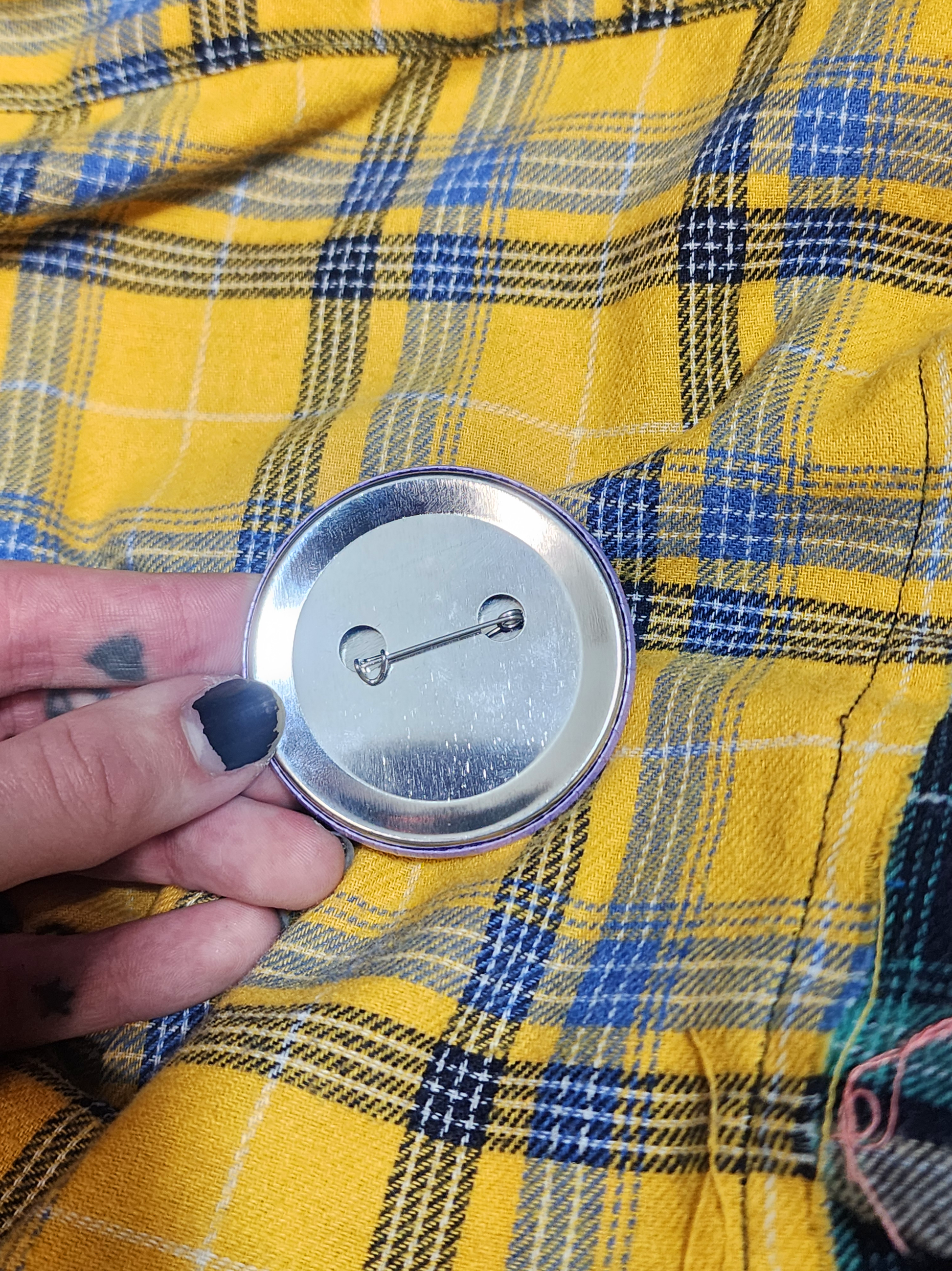 the backside of the pin against the flannel fabric in the background. the backing is metal.