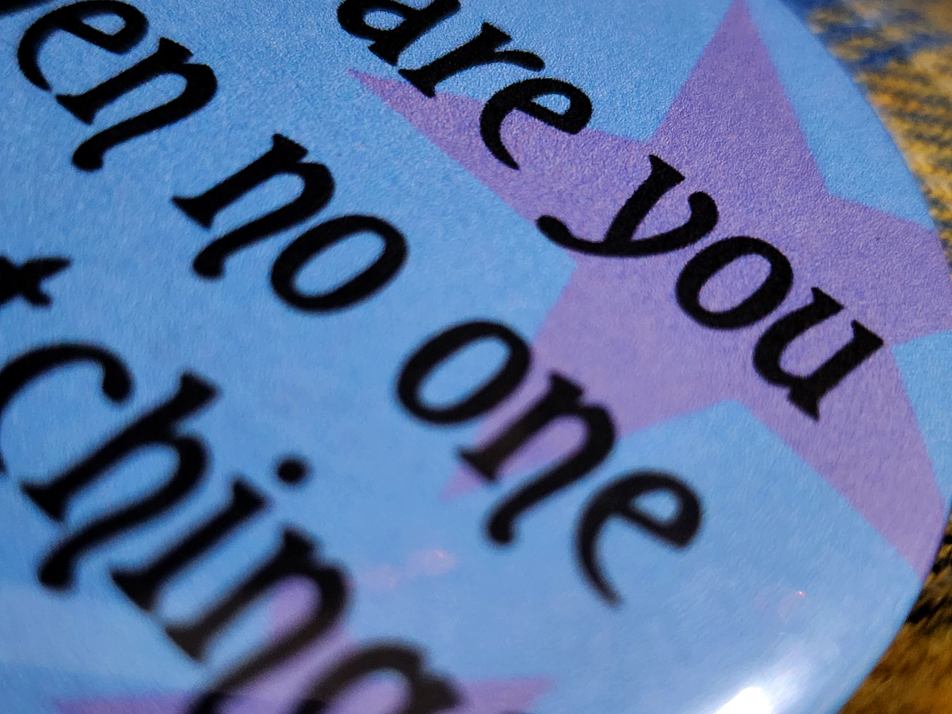 the pin sits on a yellow flannel. the pin is blue with purple decorative stars in the background. the black type reads "who are you when no one is watching?" in all lowercase letters.