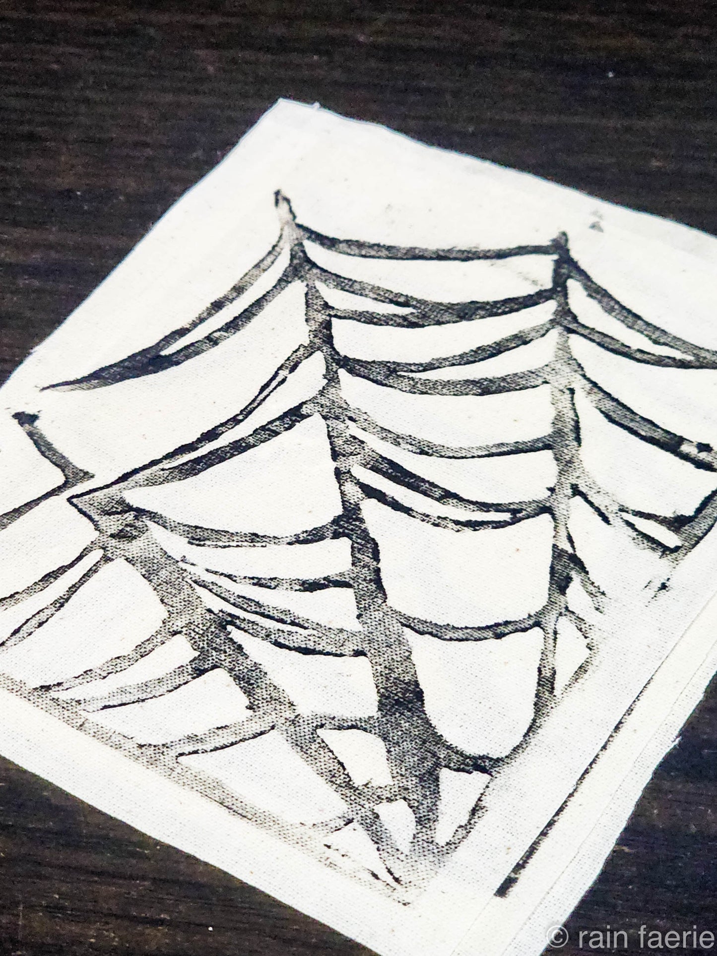 Stack of white fabric patches with a bold black linocut design of a spiderweb, printed by hand. The patches are placed on a dark wooden surface. Perfect for sewing onto crust pants, battle vests, battle jackets, or any fabric surface!!